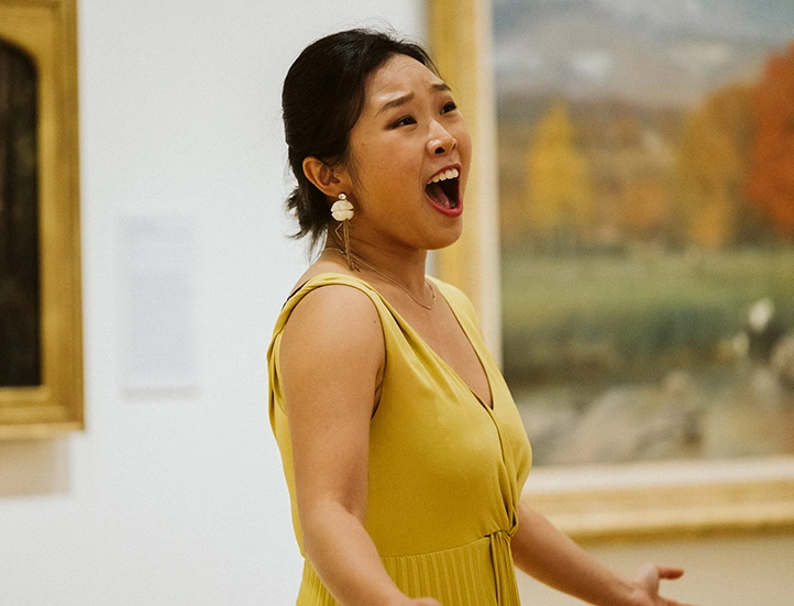 photo of a singer in a yellow dress performing in front of a painting