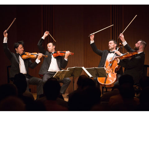 Photo of string quartet musicians wearing tuxedos on stage with their instruments wearing