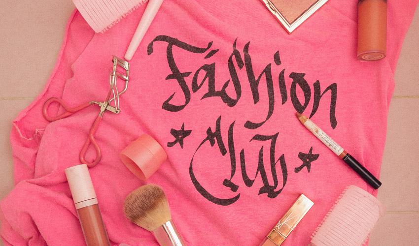 photo of hot pink shirt with the text "fashion club" in graffiti lettering and covered in makeup items against pink tiles