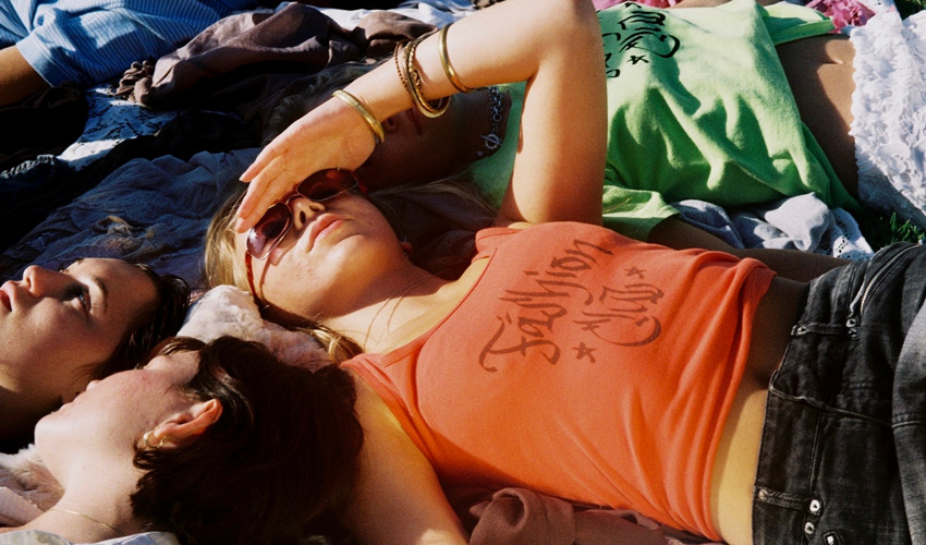 photo from above of a group of young adults facing up towards the sun lying on a blanket in a field
