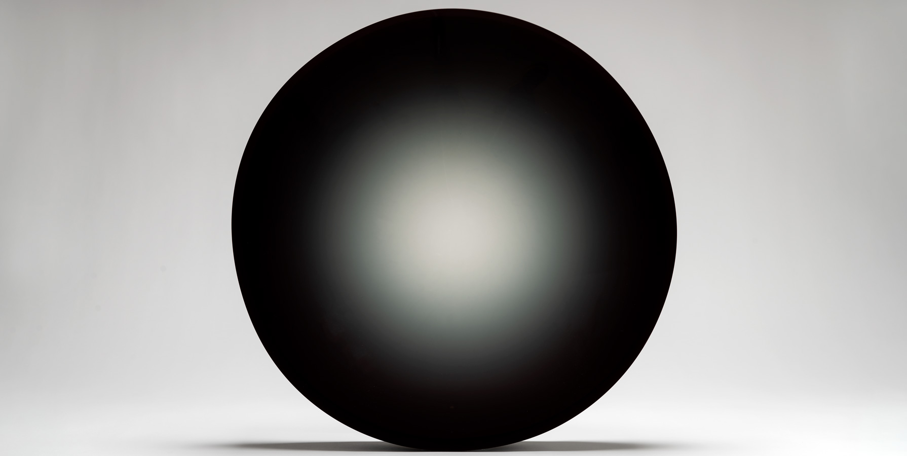 photo of dark and round work of art with a seemingly flat and shiny surface against a light gray backdrop
