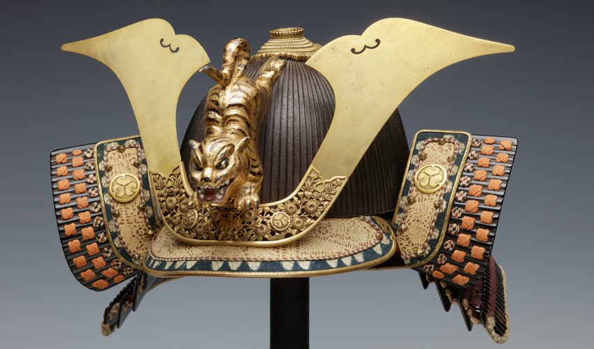 detail of a Japanese suit of armor helmet on a stand against a gray backdrop