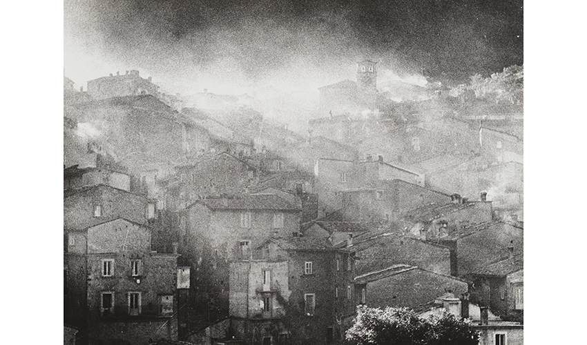black and white image of rows of brick houses with sunlight filtering through dust behind them