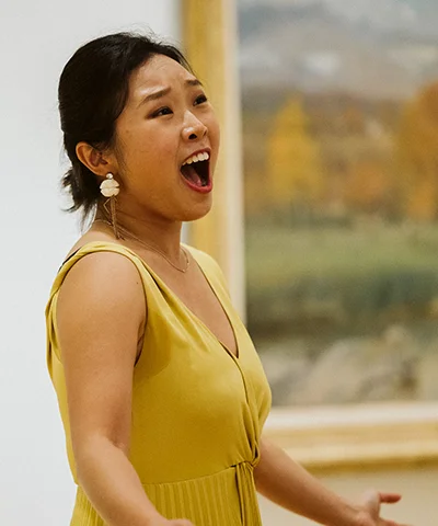 photo of a singer in a yellow dress performing in front of a painting