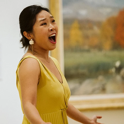 photo of a singer in a yellow dress performing in front of a painting