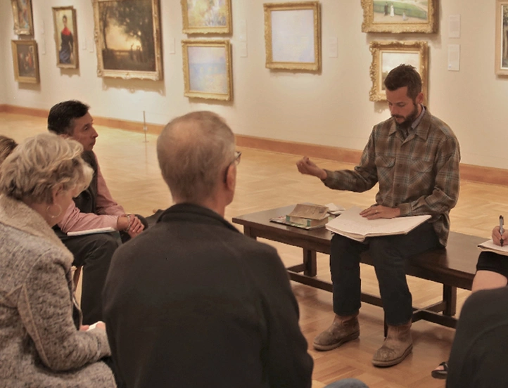 photo of people in a gallery around a person on a bench instructing