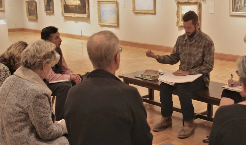 photo of people in a gallery around a person on a bench instructing