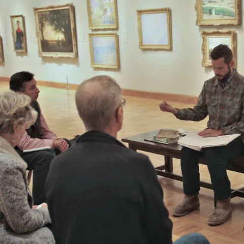 photo of people in a gallery around a person on a bench instructing