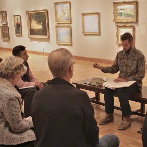 photo of people in a gallery around a person on a bench instructing