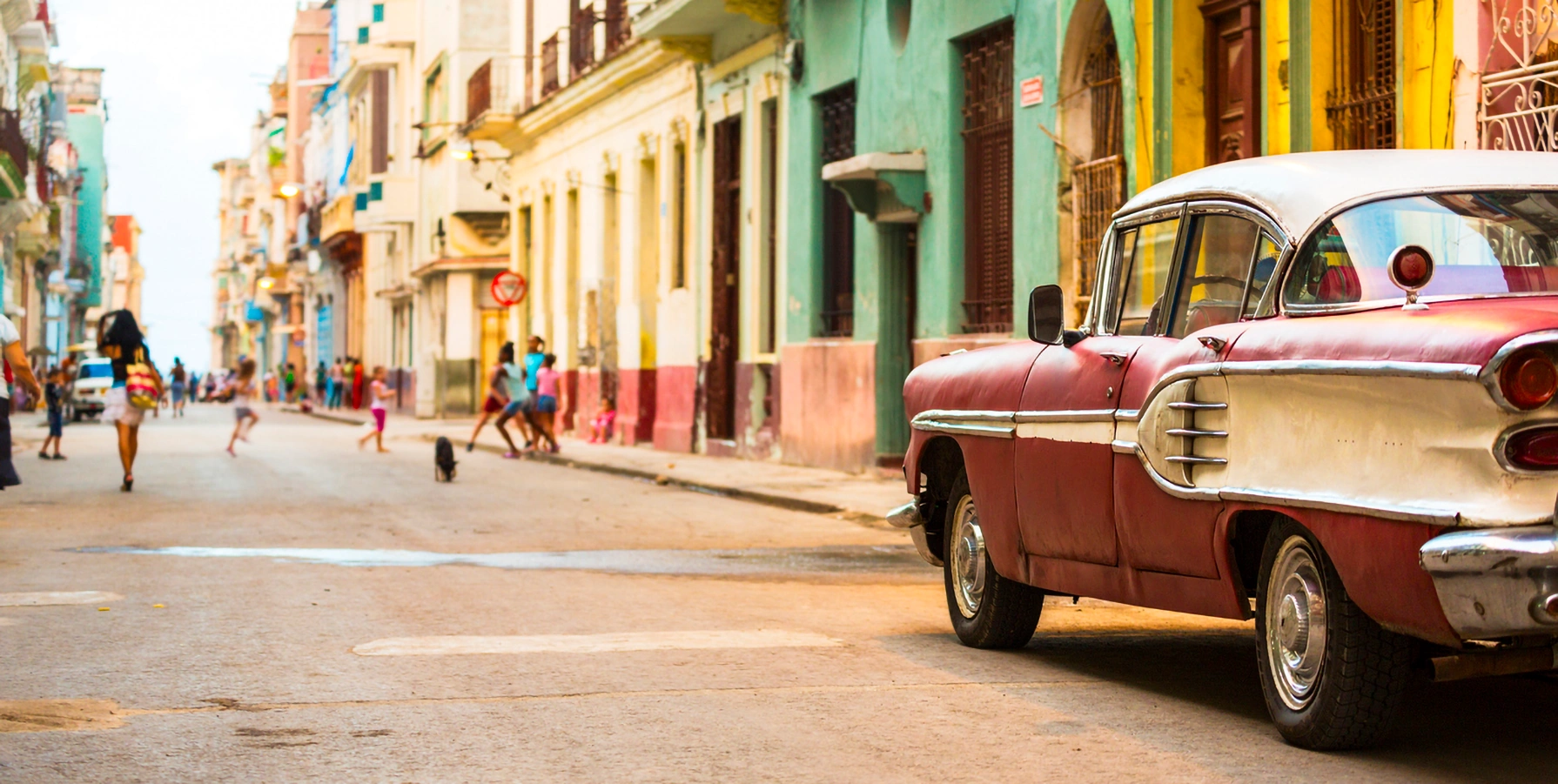 photo of old car parked on colorful street with kids playing in cuba