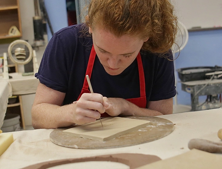 photo of student wearing a red apron crafting at a table
