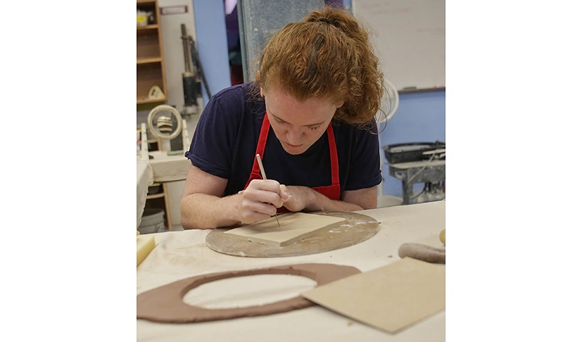 photo of student wearing a red apron crafting at a table