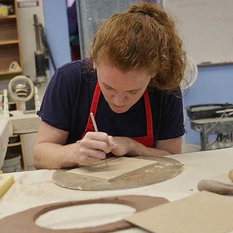 photo of student wearing a red apron crafting at a table