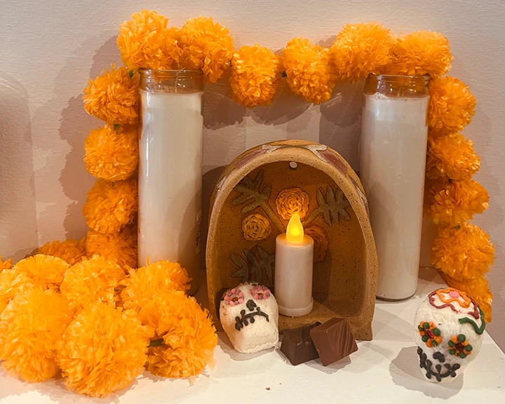 photo of dia de los muertos shrine with orange flowers surrounding white candles and a wooden arch with skulls