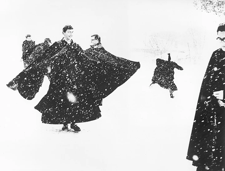 black and white photo of priests in long black cloaks playing in the snow