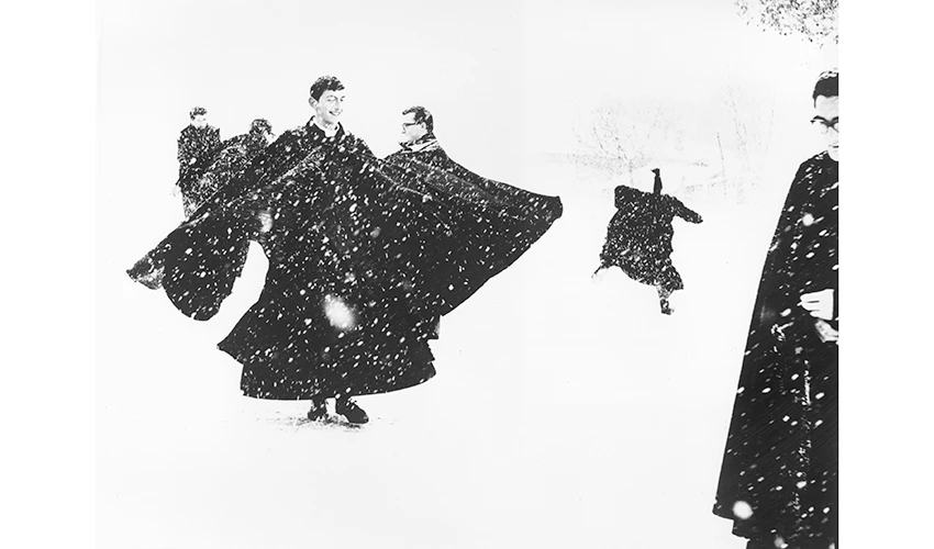 black and white photo of priests in long black cloaks playing in the snow