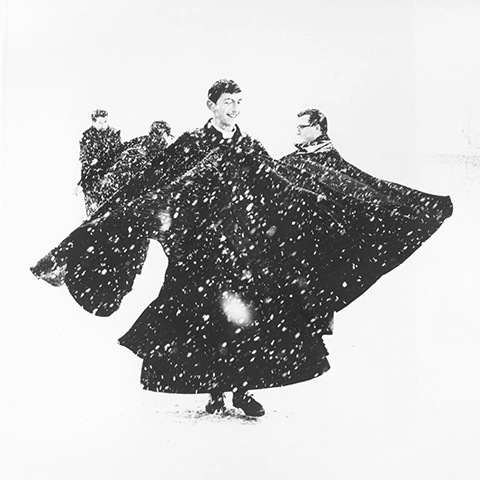 black and white photo of priests in long black cloaks playing in the snow