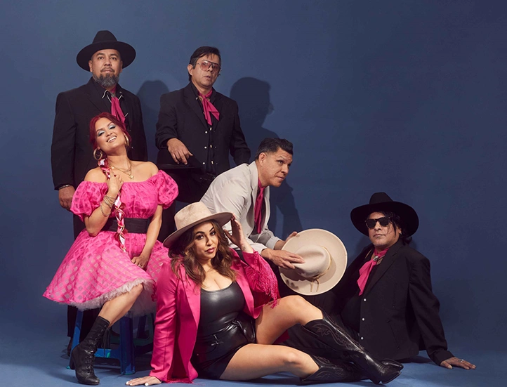 photo of musicians dressed in pink and black outfits against a dark backdrop