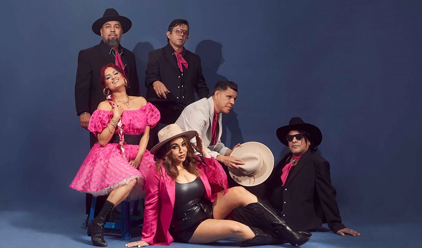 photo of musicians dressed in pink and black outfits against a dark backdrop