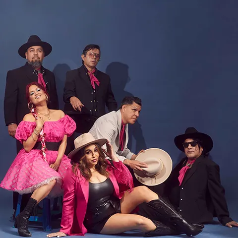 photo of musicians dressed in pink and black outfits against a dark backdrop