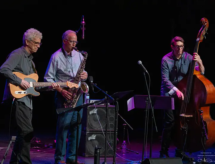 jazz trio of men including guitarist, sax player, and stand up bassist on stage playing