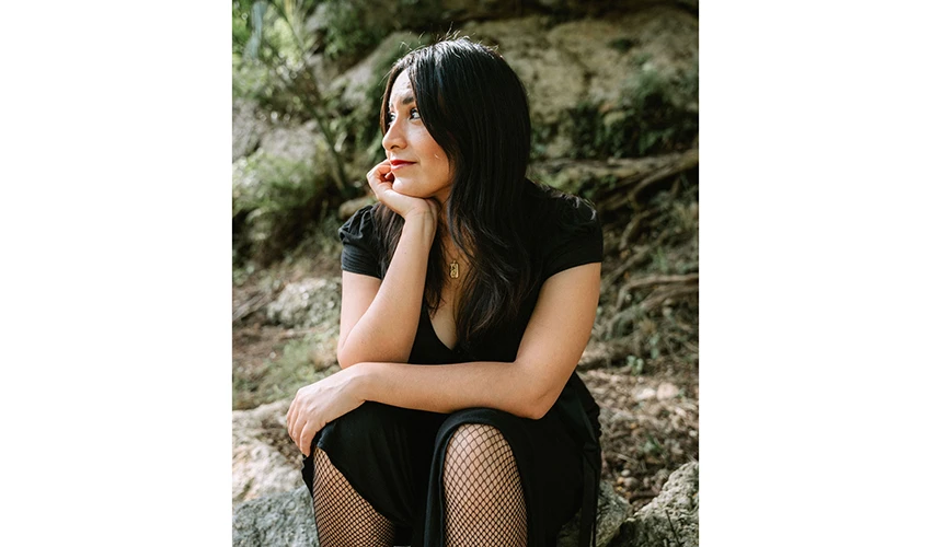 photo of presumably a woman with dark hair and a black dress siting on rocks looking to her right