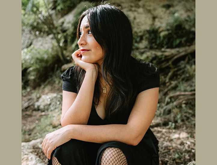 photo of presumably a woman with dark hair and a black dress siting on rocks looking to her right