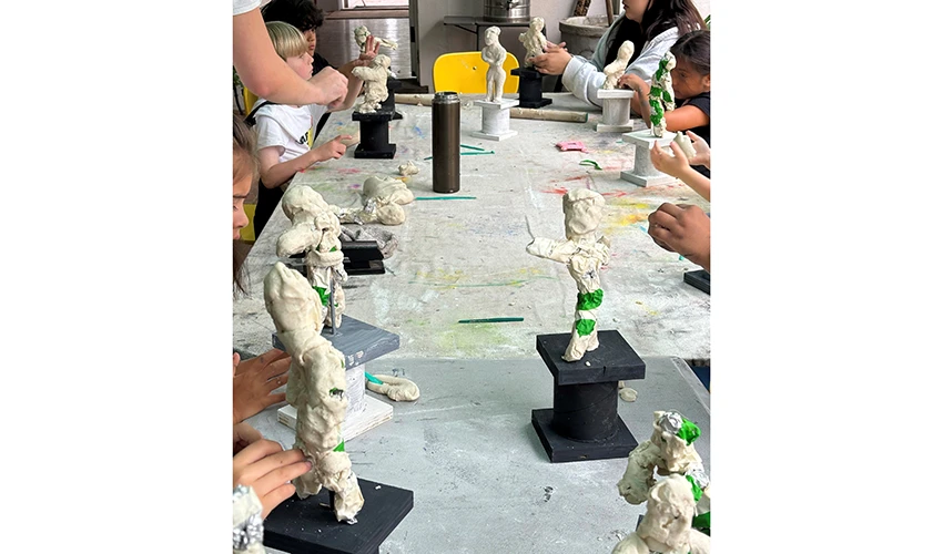 photo of white clay sculptures on a long table being crafted by kids