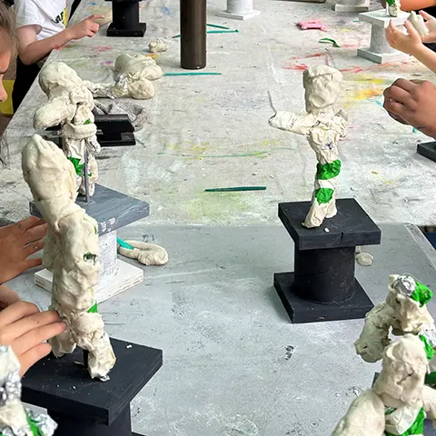 photo of white clay sculptures on a long table being crafted by kids