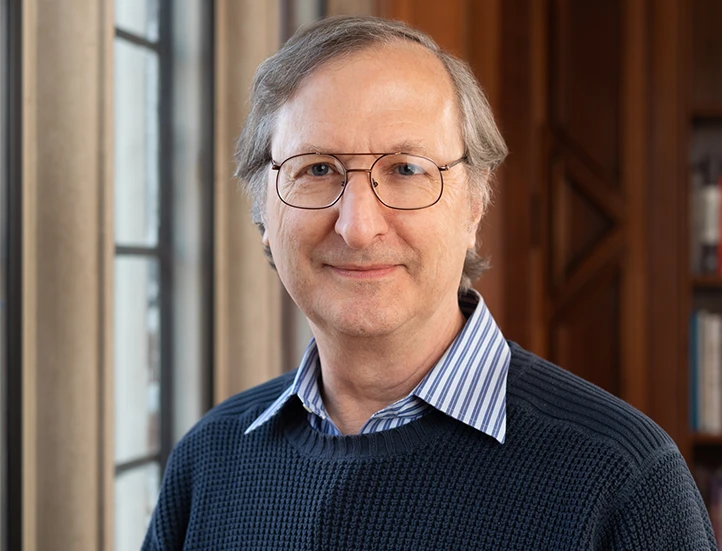 headshot of a scholar with short gray hair and glasses wearing a dark sweater over a collared shirt