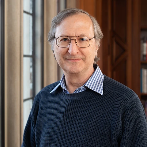 headshot of a scholar with short gray hair and glasses wearing a dark sweater over a collared shirt