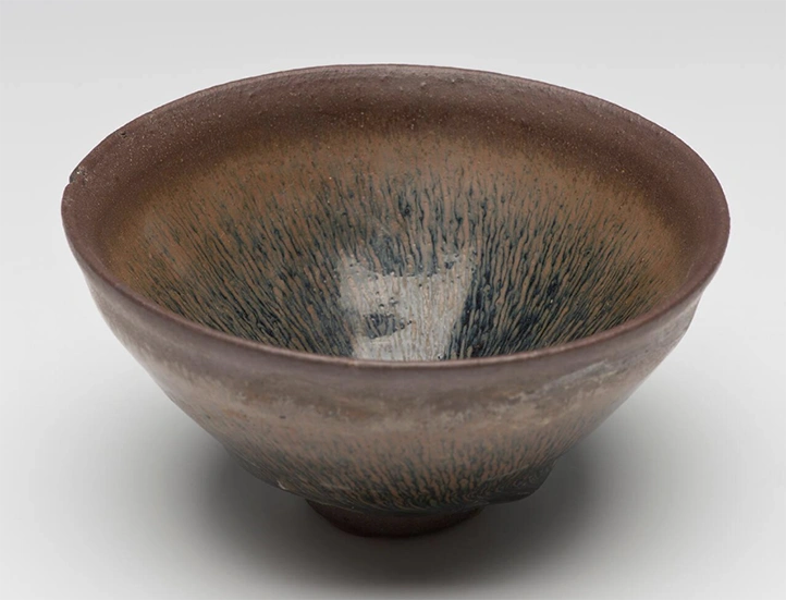 photo of a dark glazed ceramic bowl against a light gray background shot from slightly above