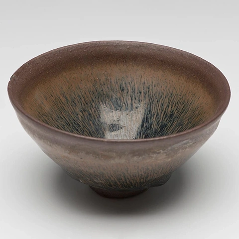 photo of a dark glazed ceramic bowl against a light gray background shot from slightly above