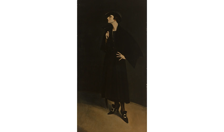 a woman in dark clothes and hat standing against a dark background looking away from the viewer