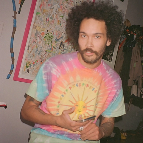 photo of the artist with a beard and wearing a tie dyed shirt looking at the camera