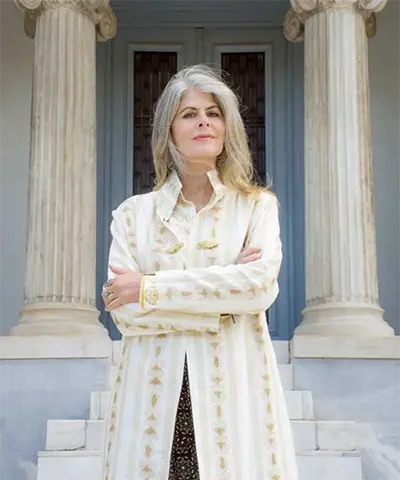 photo of a woman in a white coat with her arms crossed standing in front of an old structure with big columns