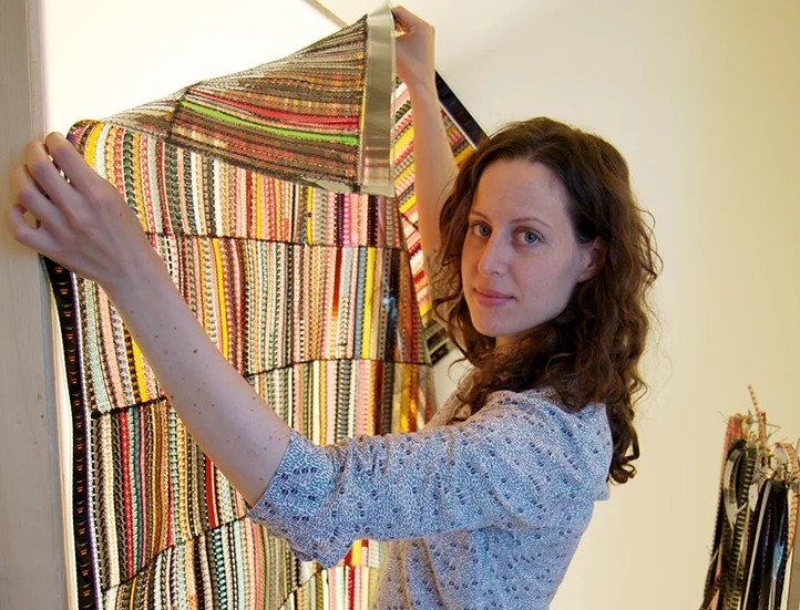 photo of an artist looking into the lens while holding up a colorful artwork against a lightbox