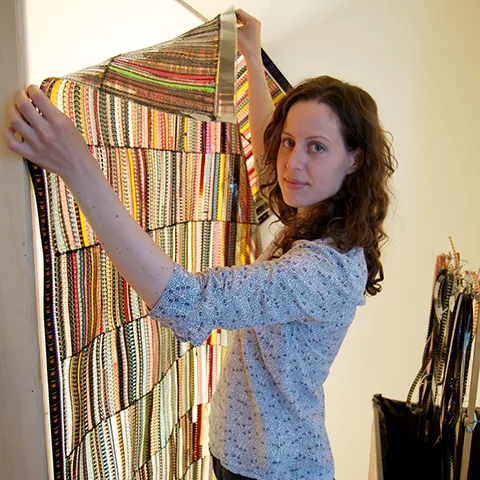 photo of an artist looking into the lens while holding up a colorful artwork against a lightbox