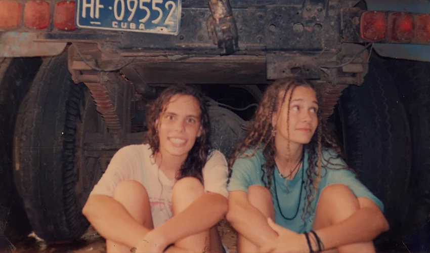 photo of two women in t shirts sitting against the back of a truck facing the camera