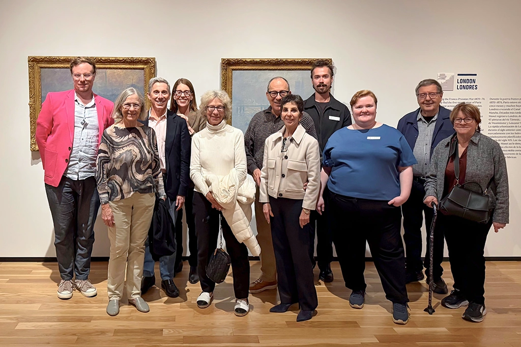 group of about 10 museum visitors posing for a picture in a gallery in front of some oil paintings