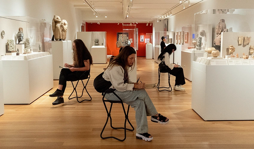 group of seated students drawing in a gallery of Asian art