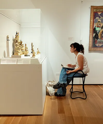 photo of a seated student sketching Asian art in a gallery