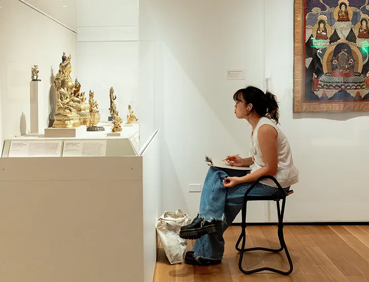 photo of a seated student sketching Asian art in a gallery