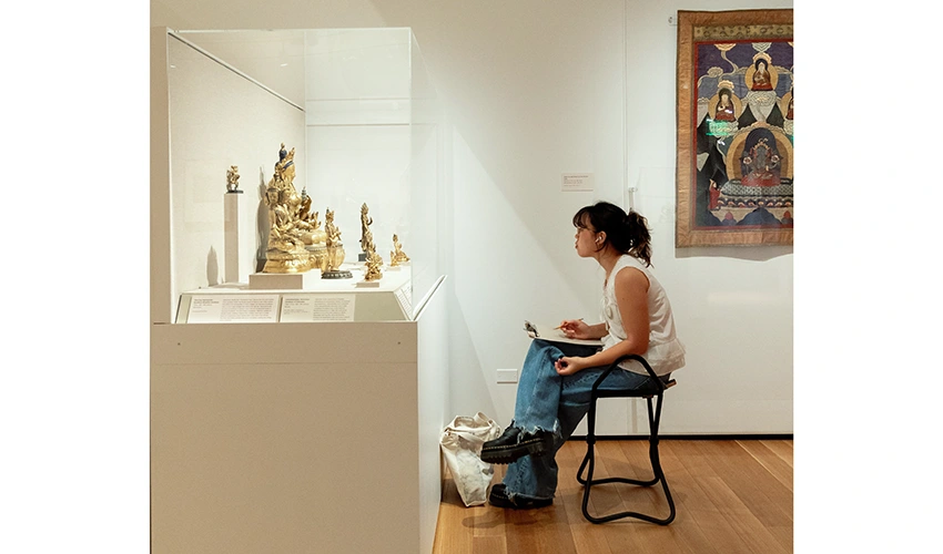 photo of a seated student sketching Asian art in a gallery