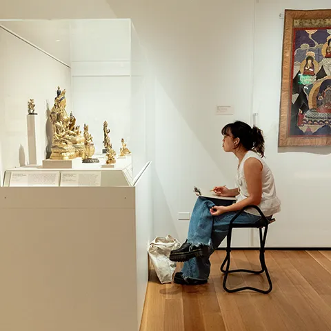 photo of a seated student sketching Asian art in a gallery