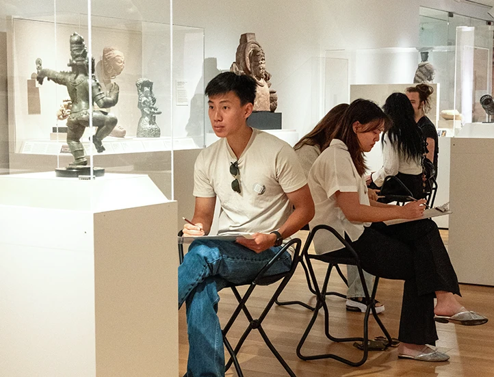 group of seated students drawing in a gallery of Asian art