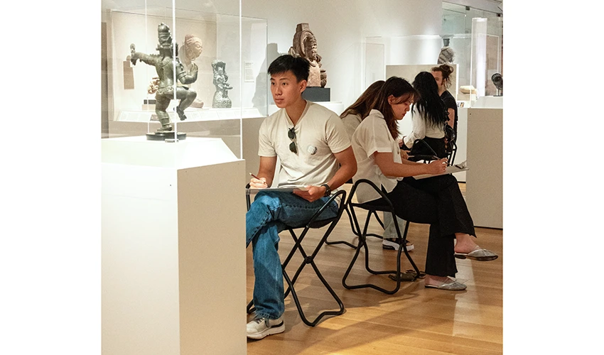 group of seated students drawing in a gallery of Asian art