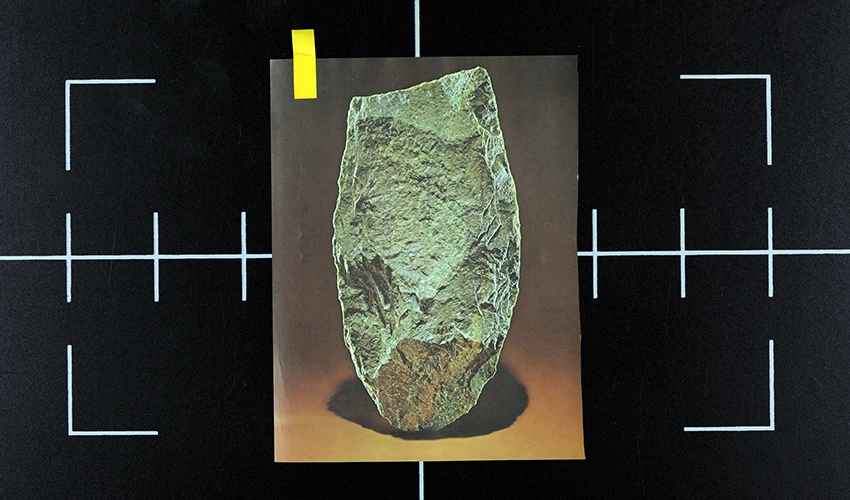 video still of a black surface with white registration marks and an image of a green stone artifact layed on top