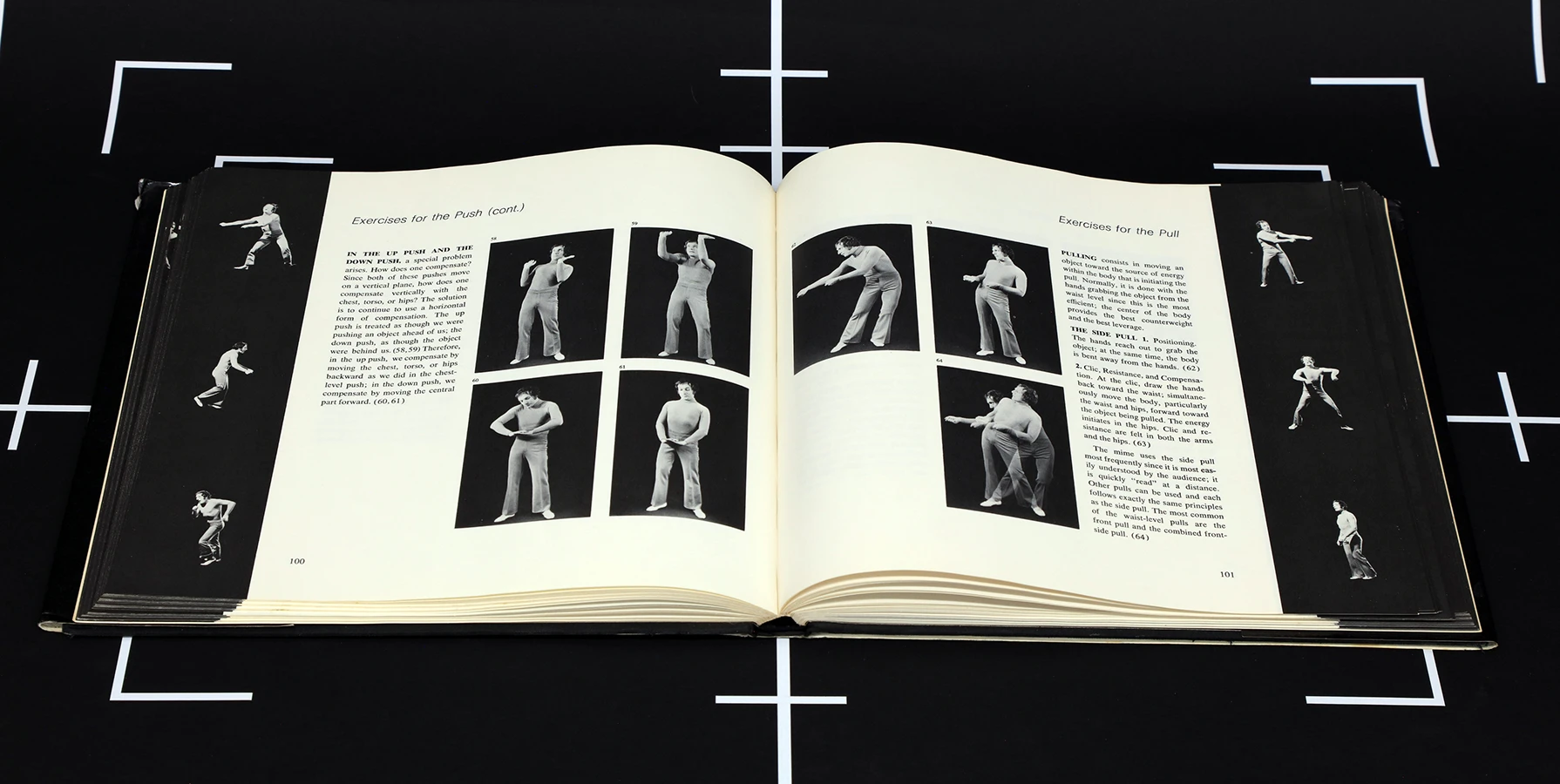 video still of a black surface with white registration marks and a book of black and white photos of a performer laid open on top
