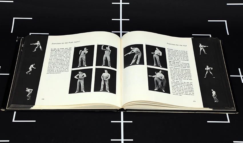 video still of a black surface with white registration marks and a book of black and white photos of a performer laid open on top